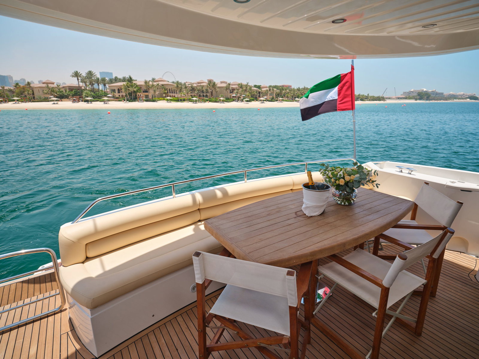 Sunseeker Satoshi 70 aft deck dining area with table seating and UAE flag overlooking turquoise water