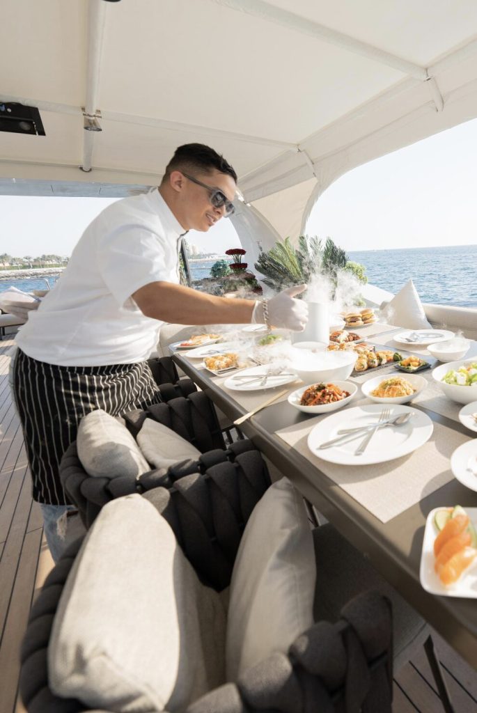 Chef preparing and serving gourmet dishes on a luxury yacht dining table at sea
