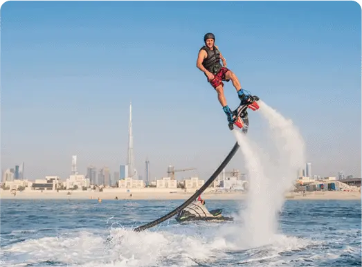 Person performing flyboarding above the water with city skyline in the background.